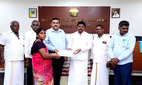 தமிழ்நாடு கட்டுமான தொழிலாளர் நலவாரிய தலைவர் பொன்குமார் ஒரு பயனாளிக்கு உதவித்தொகை வழங்கிய காட்சி. அருகில் கலெக்டர் ரவிச்சந்திரன் உள்ளார்.