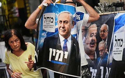 A Likud Party activist holds a campaign banner featuring Prime Minister Benjamin Netanyahu at a market in Tel Aviv, October 22, 2026, ahead of the election.