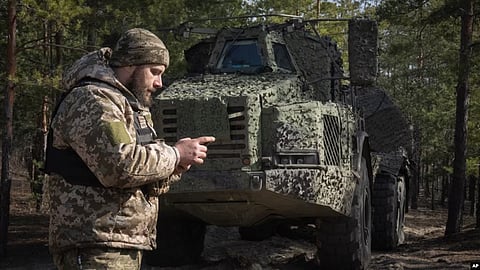 A Ukrainian soldier checks his phone while standing in front of a Swedish self-propelled Archer howitzer system