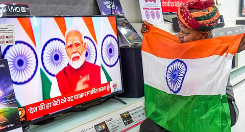 A man holds the national flag as he watches the live telecast of Prime Minister Narendra Modi's address to the Nation, in Bikaner, Monday, May 12, 2025.