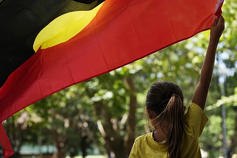 A young girl holds an Aboriginal flag at an Indigenous Australians protest during Australia Day in Sydney, Friday, Jan 26, 2024.