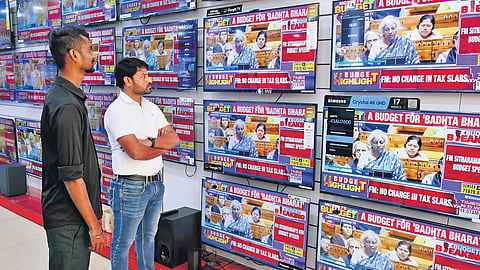 Staff of an electronics showroom keenly watch the presentation of Union Budget, in Vijayawada on Thursday
