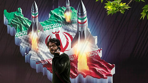 A passerby, taking his cellphone, walks past a banner showing missiles being launched from an Iranian map in northern Tehran, Iran, Friday, April 19, 2024.