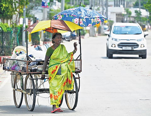 Shielded by two umbrellas, a scrap collector moves her cart on a hot, sunny afternoon in Karimnagar