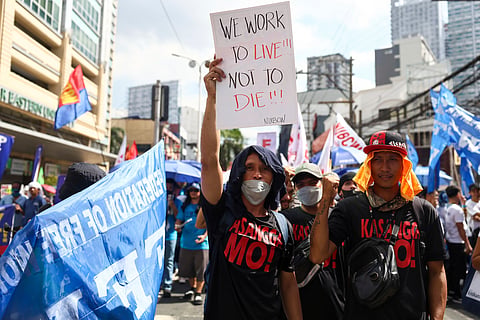 A man carries a poster during a protest to mark International Labour Day near the presidential palace in Manila, Philippines on Wednesday, May 1, 2024.