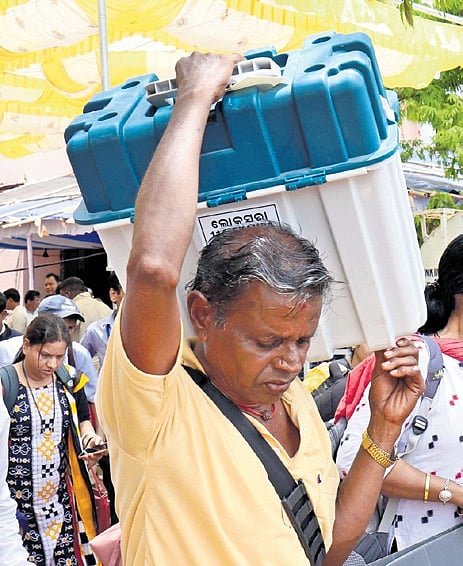 A polling staff carries an EVM to a booth in Bhubaneswar, on Friday