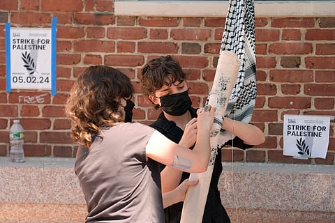 Activists attach a rolled placard to keffiyeh scarves tied together to form a line as they prepare to hoist the banner through an upper floor window to protesters occupying a portion of the building at Rhode Island School of Design, Tuesday, May 7, 2024, in Providence, R.I.