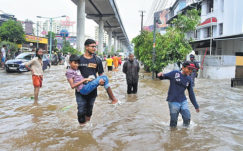 A man carries a boy while navigating a flooded street at Edappally in Kochi, as heavy rain lashed the area on Tuesday morning.