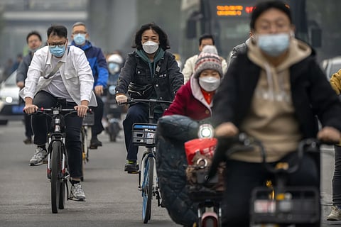 Commuters wearing face masks ride bicycles along a street in the central business district in Beijing, Thursday, October 20, 2022.