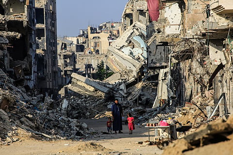 A man with his children walks past destroyed buildings in Khan Yunis on June 20, 2024, amid ongoing battles