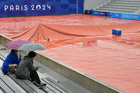 Spectators take shelter from the rain as the wet weather delays the start of play on the outside courts at the Roland-Garros Stadium at the Paris 2024 Olympic Games, in Paris on July 27, 2024.