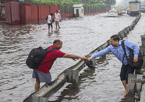 A pedestrian hands his shoes, to prevent them from getting wet, as he tries to cross a waterlogged road following rains, in Gurugram