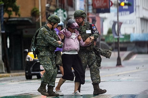 A woman is helped by military officers after falling from her motorcycle due to strong wind from Typhoon Gaemi in Keelung