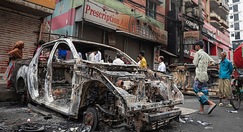 People walk past a vandalised car in Dhaka, Bangladesh, Tuesday, Aug. 6, 2024.
