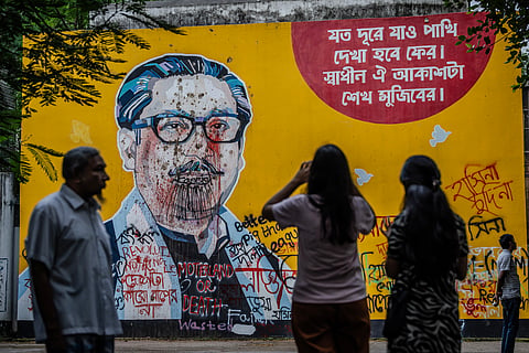 People stand and take photos in front of anti-government graffiti on a vandalised mural depicting Bangladesh's founding father Sheikh Mujibur Rahman