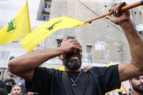 A man reacts while holding a Hezbollah flag during the funeral of people killed after hundreds of paging devices exploded in a deadly wave across Lebanon the previous day, in a south Beirut district, on September 18, 2024. Hundreds of pagers used by Hezbollah members exploded across Lebanon on September 17, killing at least nine people and wounding around 2,800 in blasts the Iran-backed militant group blamed on Israel.