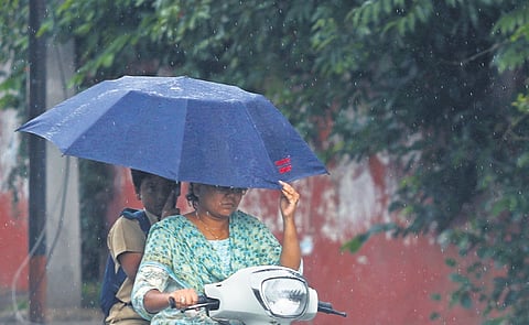 A boy shields himself and a woman from getting wet with an umbrella while she is seen riding a bike amid rains in Hyderabad on Wednesday
