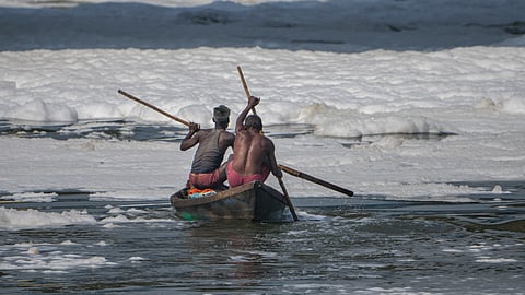 Fishermen row their boat through toxic foam in the Yamuna river on Wednesday.