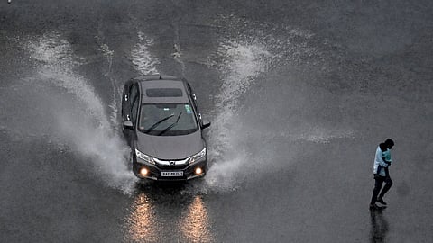 A man carrying a child walks across the road near Minsk Square during rain in Bengaluru on Tuesday.