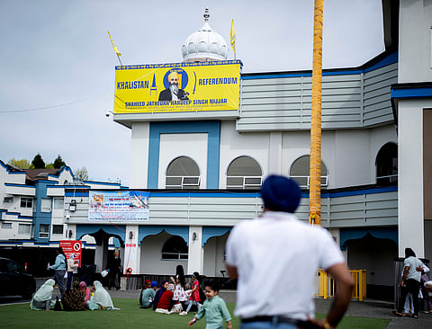 -People sit on the lawn of the the Guru Nanak Sikh Gurdwara, below a picture of Hardeep Singh Nijjar in Surrey, B.C.