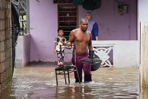 A man removes a chair and a fan from his flooded house in Tumpat, Malaysia