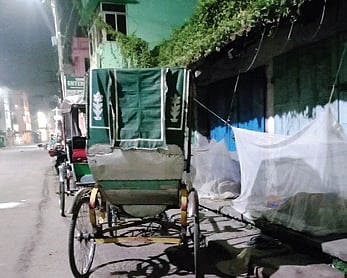 A homeless rickshaw-puller sleeping under mosquito net in front of a closed shop at Dolamundai