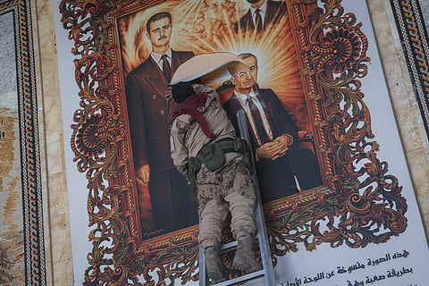 A Syrian opposition fighter tears up a painting depicting Syrian President Bashar Assad and his late father Hazef Assad at the Aleppo international airpot in Aleppo, Syria,