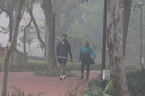 People walk in a garden during a cold and foggy winter morning, in Bhubaneswar on Saturday.