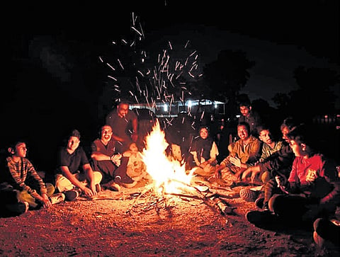 People sit around a bonfire during a night camp at Forest Trek Park, Chilkur, organised by TGFDC