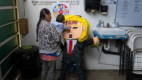 A migrant woman from the Mexican state of Guerrero holds her 1-year-old granddaughter as she hits a piñata of President Donald Trump at a shelter for migrants Wednesday, Jan. 22, 2025, in the border city of Tijuana, Mexico.
