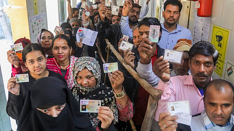 Voters show their ID cards as they wait in queues at a polling booth to cast votes during the Delhi Assembly elections, at Shahzada Bagh in New Delhi.