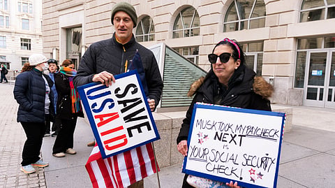 Priya Kathpal, right, and Taylor Williamson, left, who work for a company doing contract work for the United States Agency for International Development, or USAID, carry signs outside the USAID headquarters in Washington