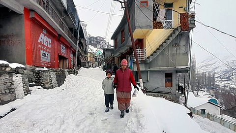 A woman with her child walks through a snowy road in Lahaul Spiti on Thursday.