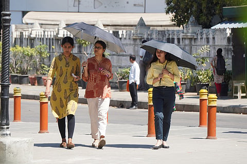 People crossing road holding umbrellas to protect themselves from hot weather near Queens road in Bengaluru.