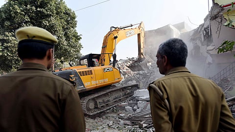 In this March 2, 2023 photo, police stand guard as a Prayagraj Development Authority bulldozer demolishes a two-story house linked to a gun store owner allegedly close to mafia-politician Atiq Ahmad in Chakiya, Prayagraj.