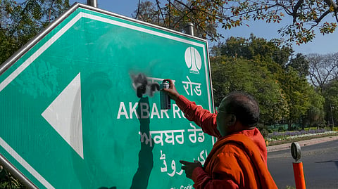 A protestor defaces the signboard of 'Akbar Road' demanding that the road be renamed after Maharishi Valmiki, in New Delhi.