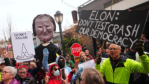 People wave signs and a during a protest against Tesla and Elon Musk outside of a Tesla showroom Saturday, March 29, 2025, in the University District of Seattle.