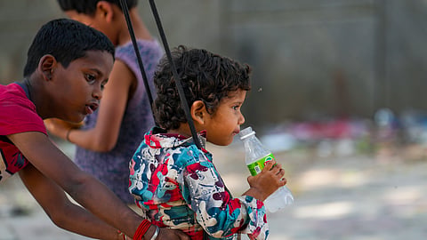 A child sips a soft drink while riding a swing during a hot summer afternoon, in New Delhi