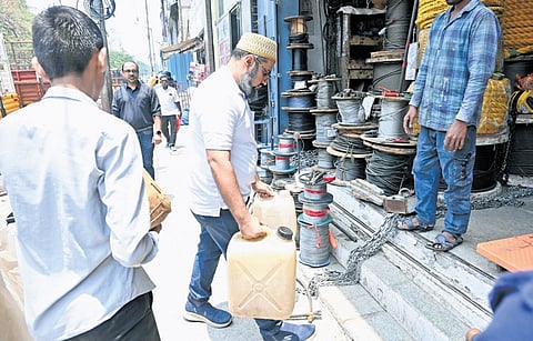 A shop owner carries water cans to his store on SJP Road as broken BWSSB pipelines have led to water scarcity in the area