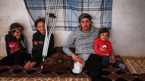 Suleiman Khalil, 21, who lost his leg in a landmine explosion while harvesting olives with his friends in a field, poses for a picture with his siblings, from left to right, Sakina, 8, Nahla, 9, and Aya, 5, at his home in the village of Qaminas, east of Idlib, Syria, Wednesday, April 9, 2025.