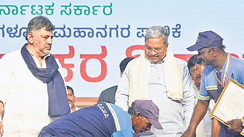 Civic workers seek Chief Minister Siddaramaiah’s blessings, as Deputy Chief Minister DK Shivakumar looks on, at an event on Palace Grounds on Thursday