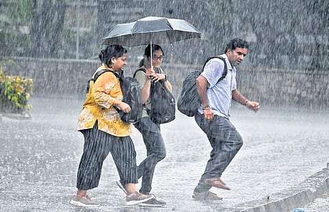 Pedestrians brave heavy rain while crossing a street, as downpour leads to waterlogged roads during peak hours in Bengaluru.
