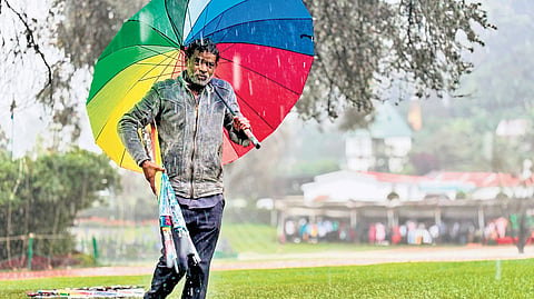 An umbrella seller shields himself from sudden showers in Ooty on Friday