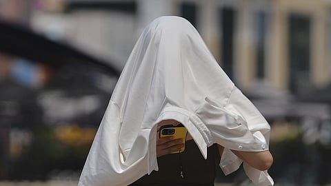 A woman covers herself from the sun as she browses a smartphone on a street during a hot day in Beijing, Wednesday, July 23, 2025.
