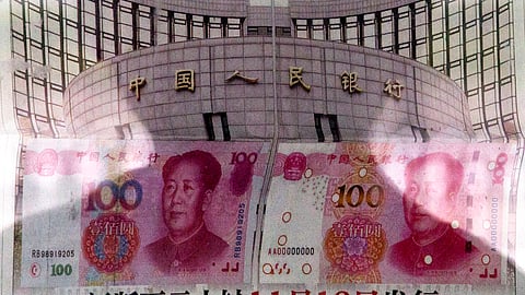 In this Aug. 11, 2015 photo, a shadow of a man is reflected on a glass as he reads a newspaper reporting China's central bank or People's Bank of China announced the 2015 edition of the 100 renminbi notes will be issued starting from November 12, at a stand in Beijing