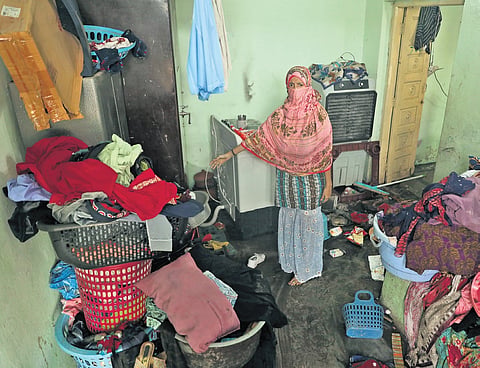 A woman points to items damaged by the flash flood in Warsiguda.
