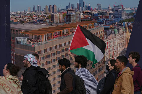 Students walk past a poster of the skyline of London as they take part in demonstration holding banners, placards and flags during an Inter-university march for Gaza in London, Tuesday, Oct. 7, 2025.