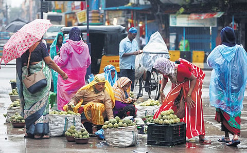 Fruit vendors shield themselves from the rain with plastic sheets at Monda Market in Secunderabad on Wednesday