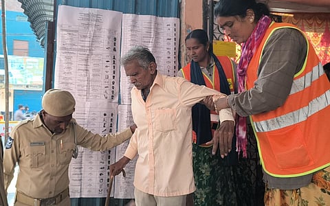 GHMC workers and police personnel help an elderly man leave the polling booth after he casts his vote at the Municipal Community Hall near Rahmatnagar Junction in Hyderabad.