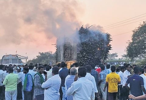People look on as smoke rises from a tractor laden with sugarcane at a sugar factory in Mudhol on Thursday